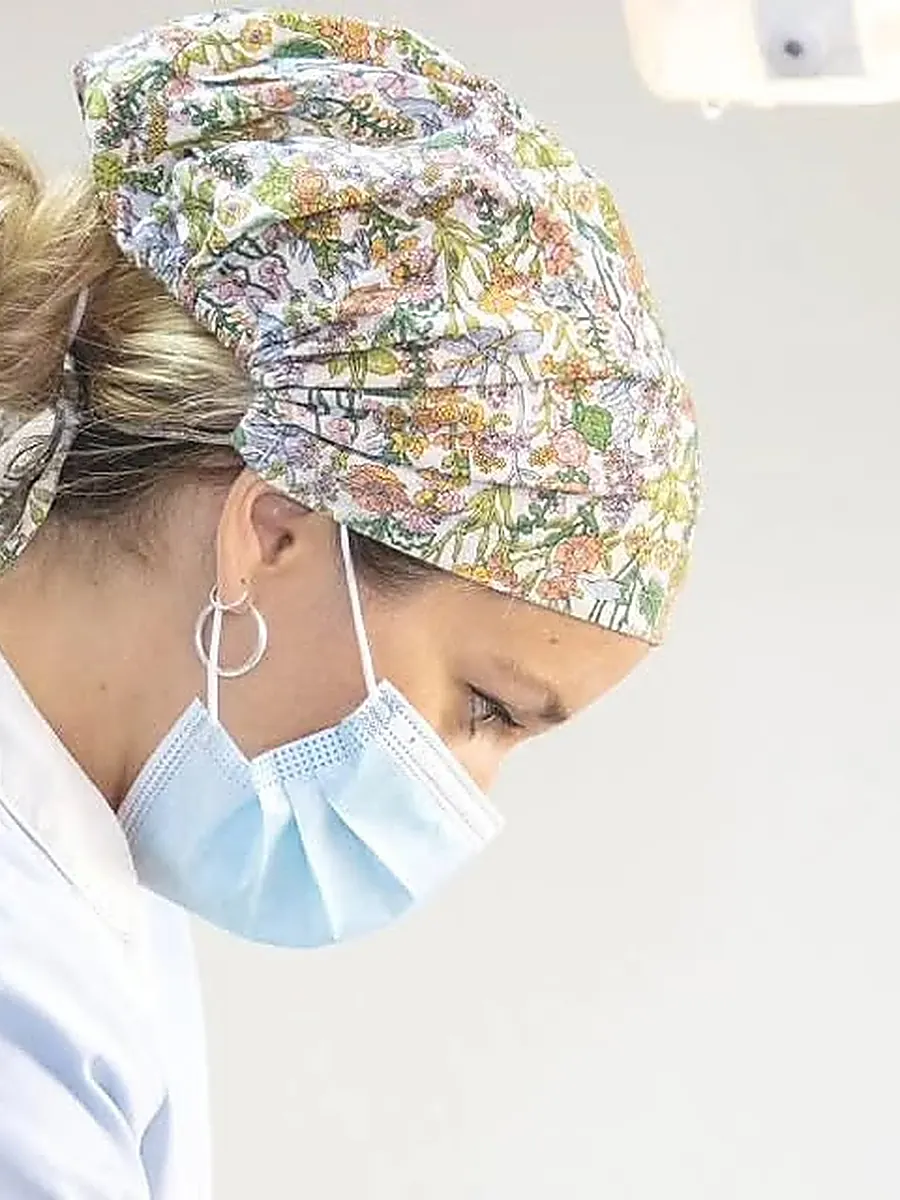 Odontóloga de Unidad Odontológica Andina, con gorro quirúrgico de flores y mascarilla, concentrada durante un procedimiento.